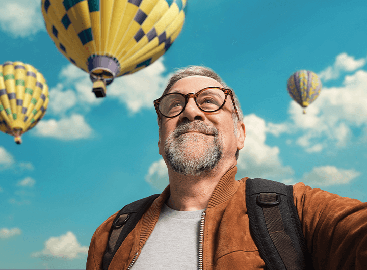 Man smiling at the sky with hot air balloons in the background