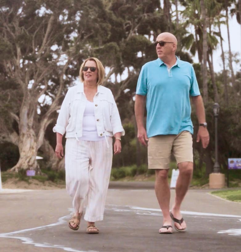 Woman in white shirt and pants walking with man in blue shirt and khaki shorts