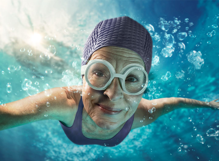 Woman swimming with purple bathing suit and water cap with purple background