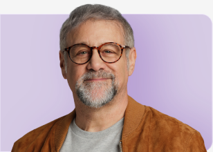 Man smiling in brown suede jacket and grey t-shirt with purple background